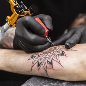 Process of creating tattoo in form of black flower. Master does work in sterile gloves