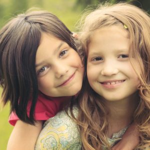 "Two cute young girls playing piggy back, looking at the camera. Similar images."