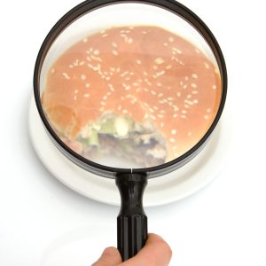 person inspecting a hamburger with a magnifying glass