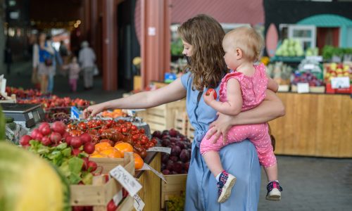 Woman buying vegetables with baby girl on farmers food market