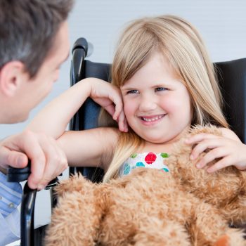 Laughing little girl sitting on the wheelchair at the hospital