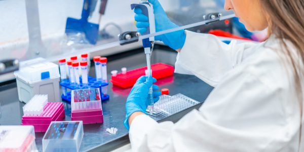 Rear view close-up of a female biologist pipetting liquid in a biosafety cabinet