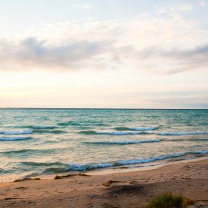 Serene sunrise beach scene along great lakes shoreline. Soft pastel hues and gentle waves invite tranquility and natural splendor.